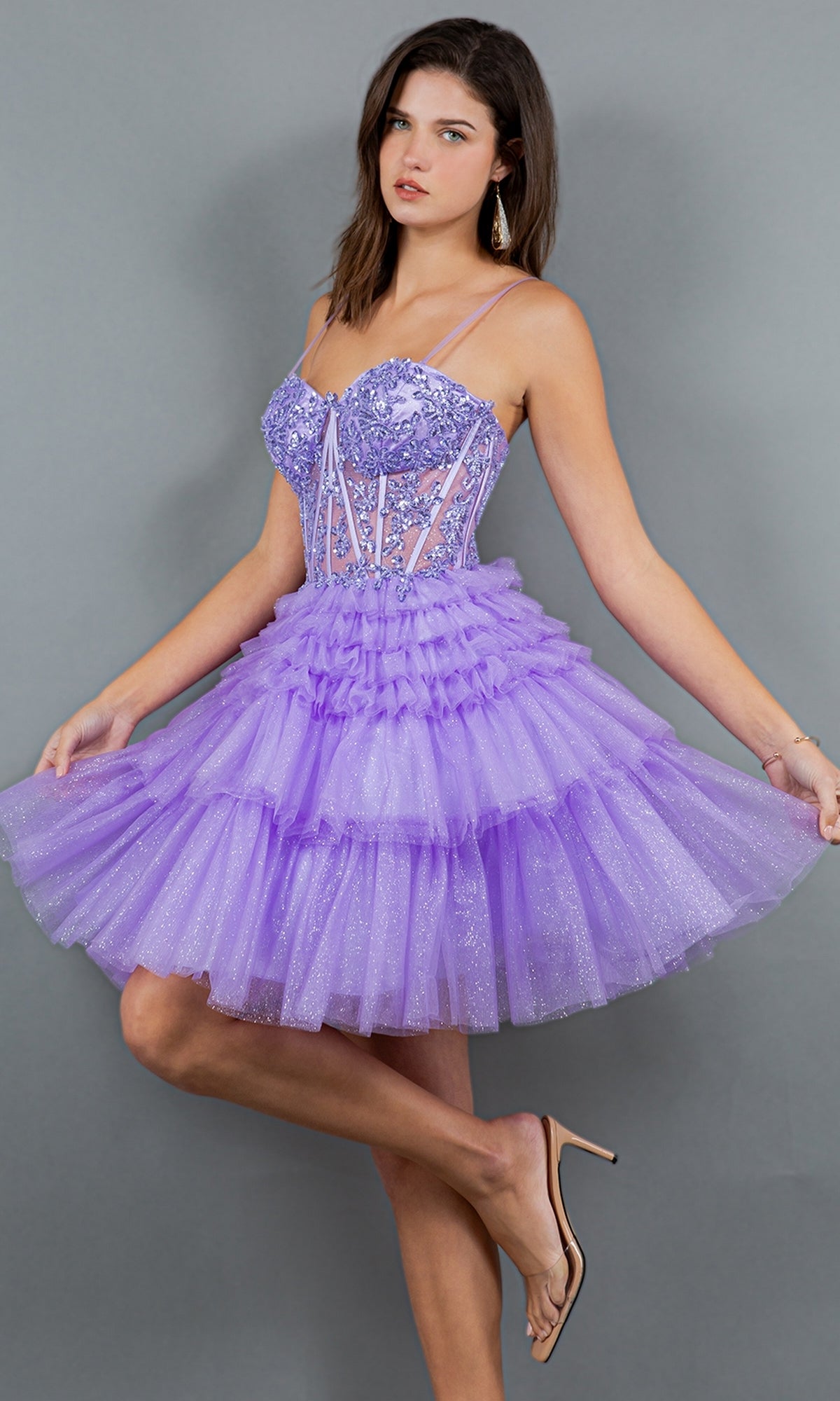A woman poses in the Short Sweetheart Ruffled Homecoming Dress 5133J, a lavender tulle A-line semi-formal dress with floral embroidery and spaghetti straps, holding out the skirt against a plain gray background.